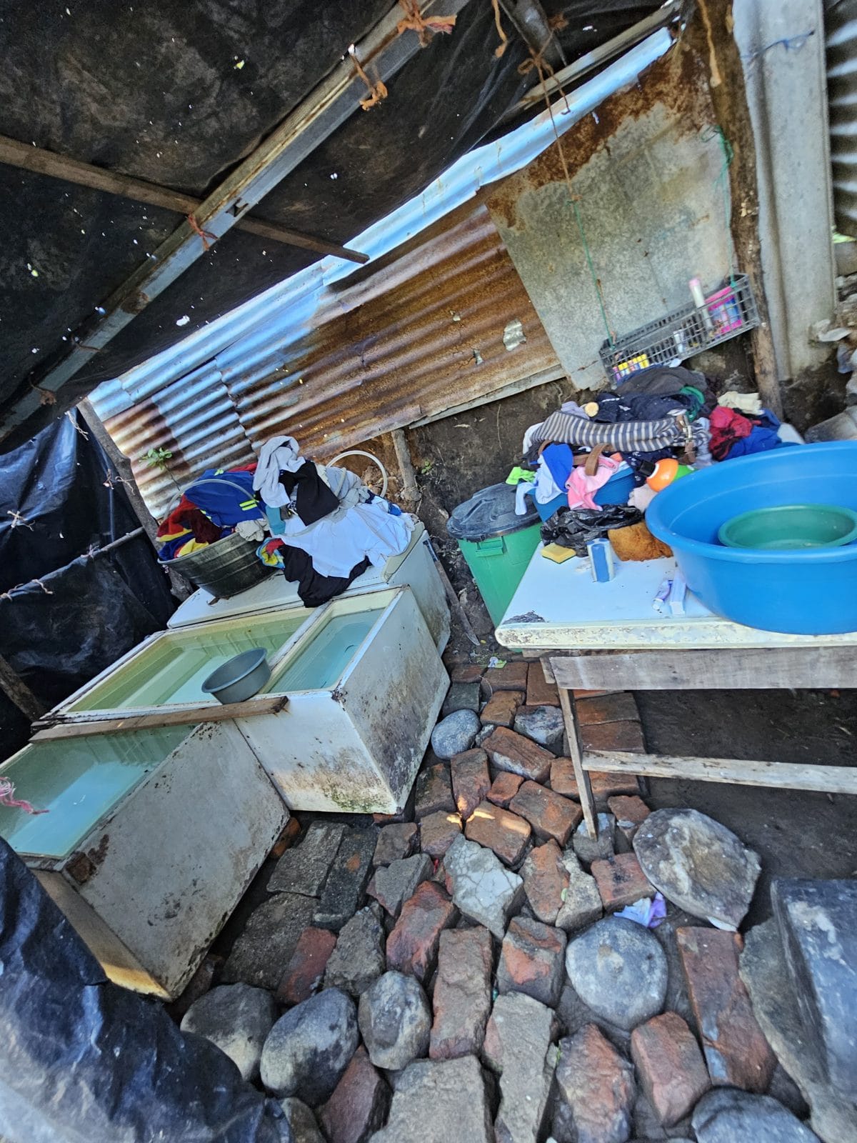 Inside one of the huts — scrap metal, tarps, stone, and everything a family owns